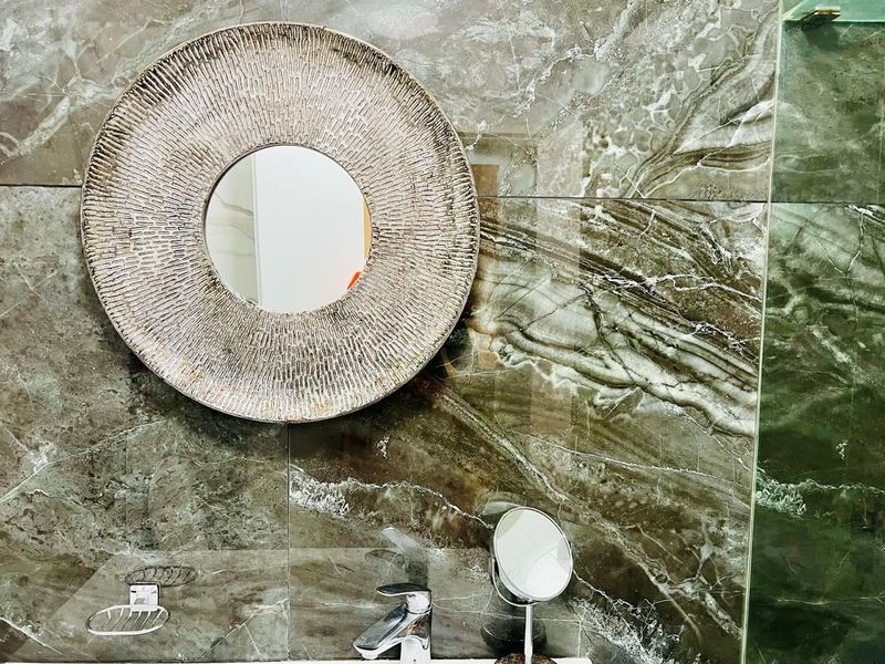 A modern bathroom featuring high-end large format marble-look wall tiles, a sleek chrome basin mixer, and a glass shower screen.