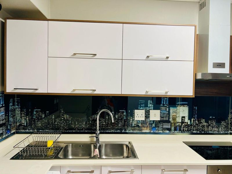 Modern kitchen featuring white cabinetry, stone countertops, a stainless steel sink, and a distinctive city-scape printed glass splashback.