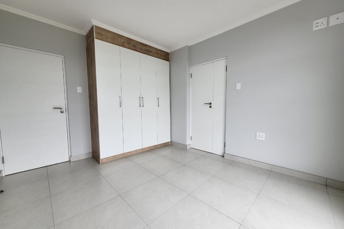 A clean, modern bedroom featuring neutral tiled flooring, light grey walls, and ample built-in cupboard storage.