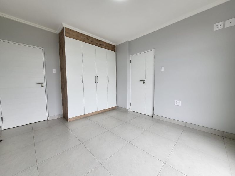 A clean, modern bedroom featuring neutral tiled flooring, light grey walls, and ample built-in cupboard storage.