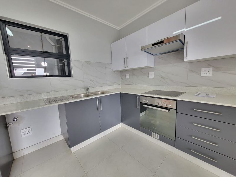 Modern kitchen featuring sleek two-tone cabinetry, stone countertops, integrated electric hob, oven, and extractor fan with neutral tiled finishes.