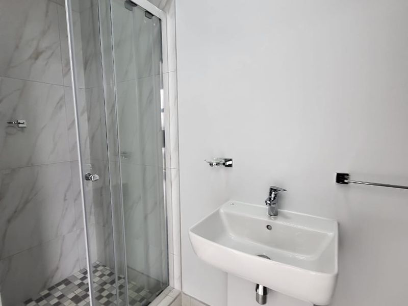 A clean, modern bathroom featuring a pedestal basin, a glass-enclosed shower with marble-look wall tiles, and neutral floor tiling.