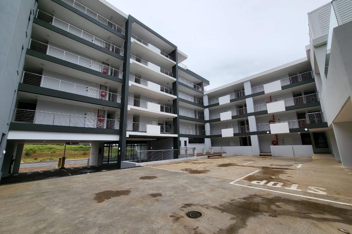 Exterior view of a modern multi-story apartment complex featuring concrete paving, balconies with stainless steel balustrades, and visible fire safety equipment.