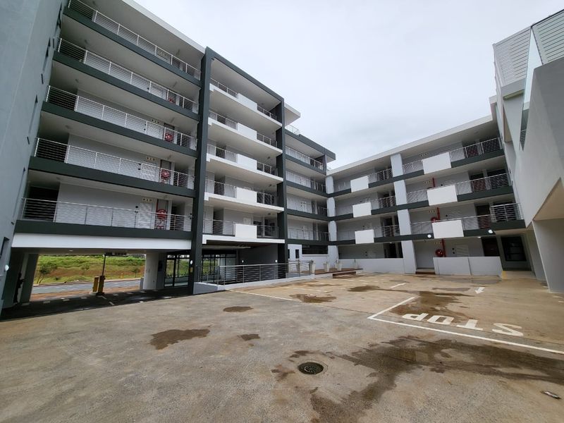 Exterior view of a modern multi-story apartment complex featuring concrete paving, balconies with stainless steel balustrades, and visible fire safety equipment.