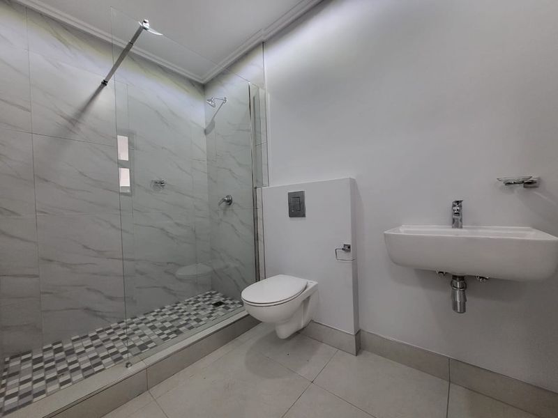 Modern bathroom featuring a walk-in shower with glass screen, wall-mounted toilet, and a sleek wall-mounted basin with contemporary chrome fixtures.
