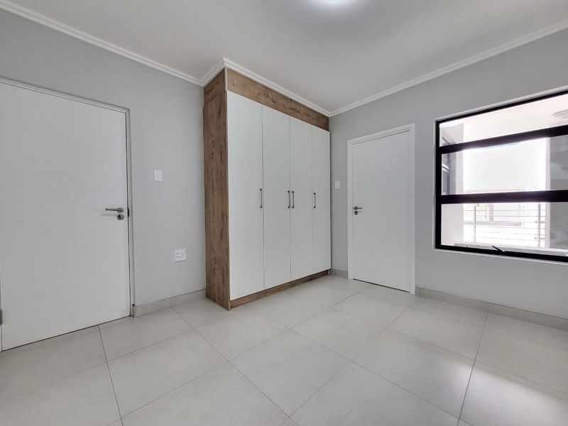 A bright, empty bedroom featuring neutral tiled flooring, a modern built-in wardrobe with wood-grain accents, and clean white walls.