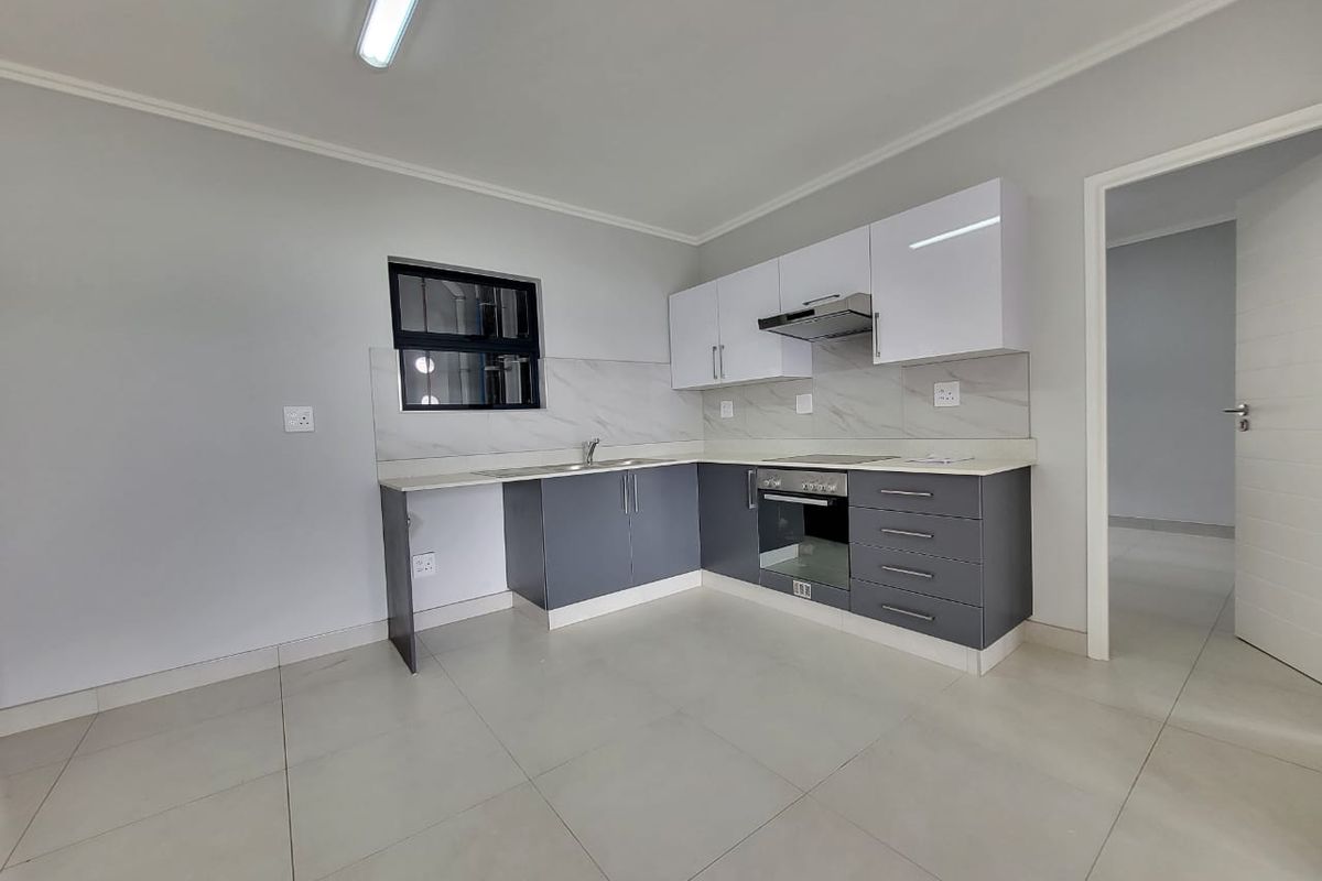 Modern kitchen featuring sleek grey and white cabinetry, stone countertops, integrated oven and hob, and neutral tiled flooring in a clean, open-plan layout.