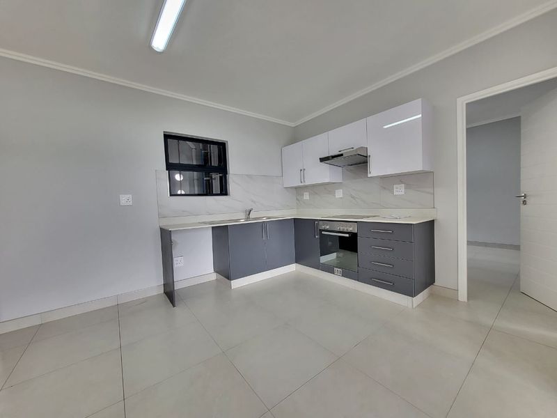Modern kitchen featuring sleek grey and white cabinetry, stone countertops, integrated oven and hob, and neutral tiled flooring in a clean, open-plan layout.