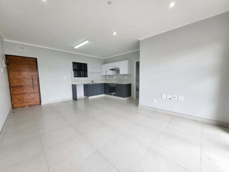 Modern open-plan living area featuring a sleek kitchen with built-in cabinetry, integrated appliances, and neutral tiled flooring throughout.
