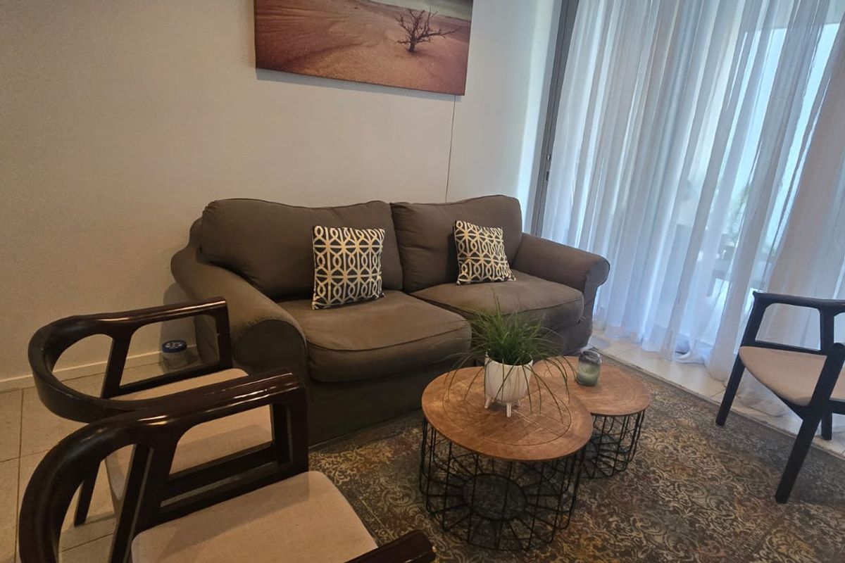 A comfortable living room area featuring tiled flooring and large sliding glass doors with sheer curtains, providing access to the outdoor space.