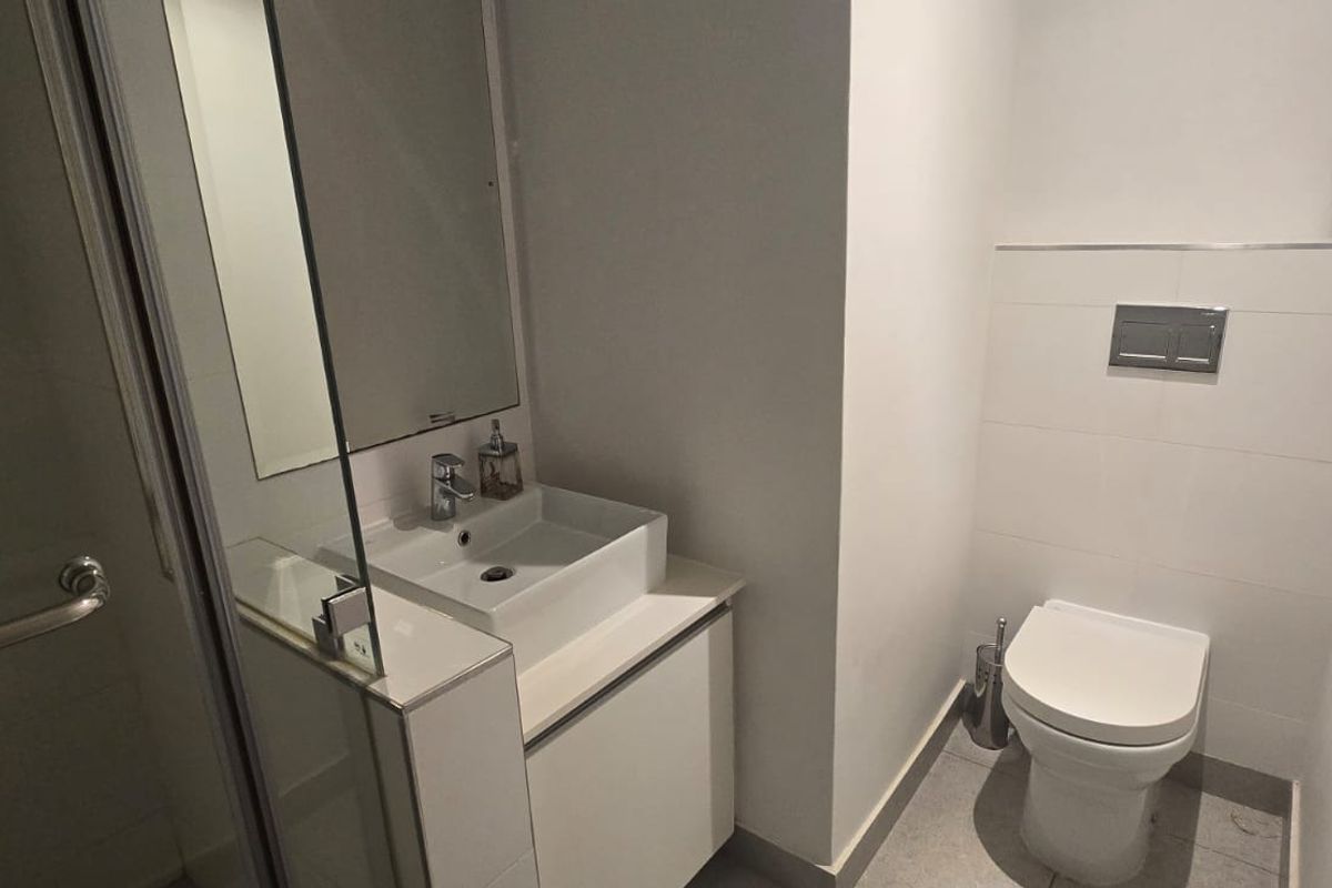 A modern bathroom featuring a wall-mounted toilet, a sleek vessel sink with vanity storage, and a glass-enclosed shower area.