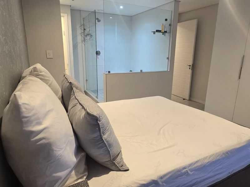 Modern bedroom featuring built-in cupboards, tiled flooring, and an en-suite glass-enclosed shower area, offering a contemporary open-concept layout.