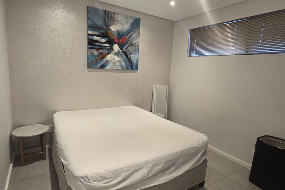 A neutral-toned bedroom featuring tiled flooring, recessed downlighting, and horizontal window blinds, offering a clean and functional living space.