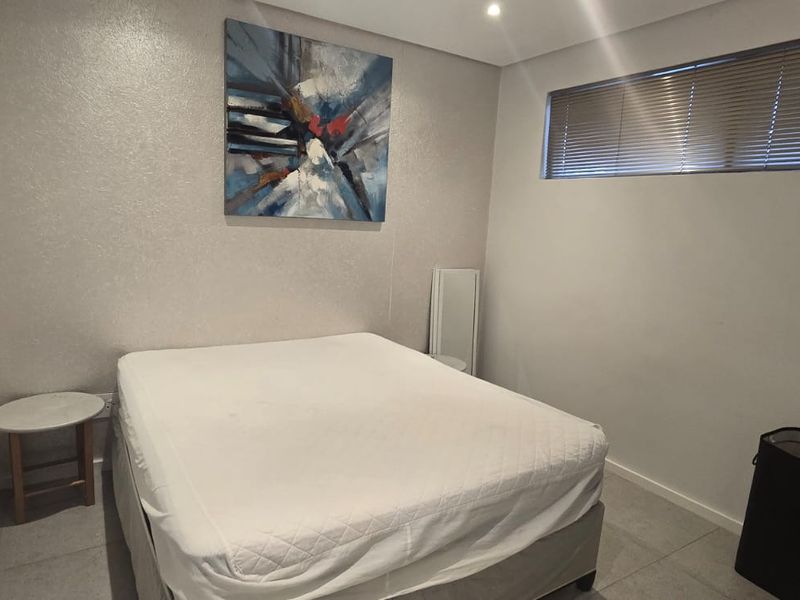 A neutral-toned bedroom featuring tiled flooring, recessed downlighting, and horizontal window blinds, offering a clean and functional living space.