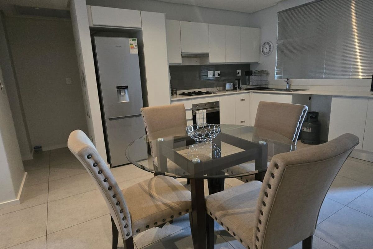 Modern open-plan kitchen featuring white cabinetry, integrated appliances, and tiled flooring, seamlessly flowing into the dining area.
