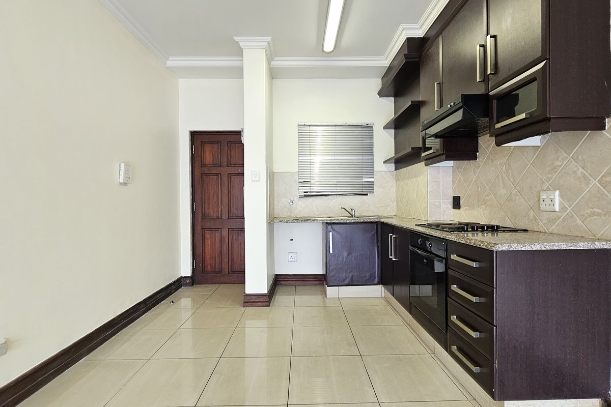 A functional kitchen featuring dark wood cabinetry, granite countertops, built-in oven and hob, tiled backsplash, and neutral floor tiles.