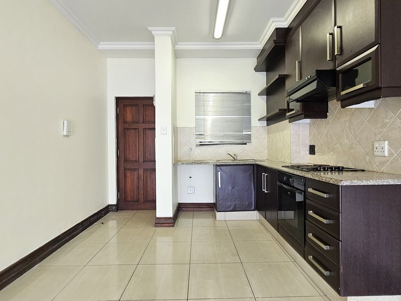 A functional kitchen featuring dark wood cabinetry, granite countertops, built-in oven and hob, tiled backsplash, and neutral floor tiles.