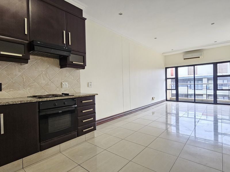 Spacious open-plan living area featuring a modern kitchen with dark cabinetry, granite countertops, tiled flooring, and sliding doors leading to a balcony.