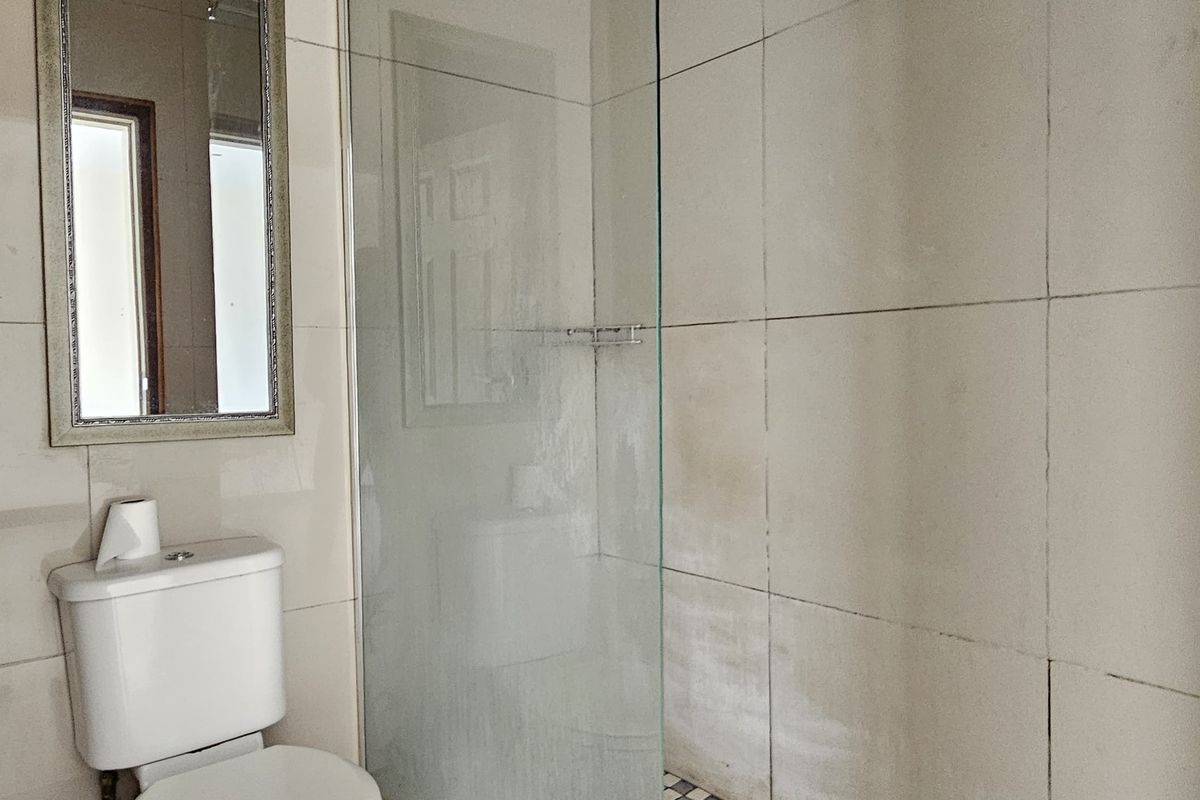 A functional bathroom featuring a glass-enclosed shower with a rainfall shower head, tiled walls, and a standard toilet.