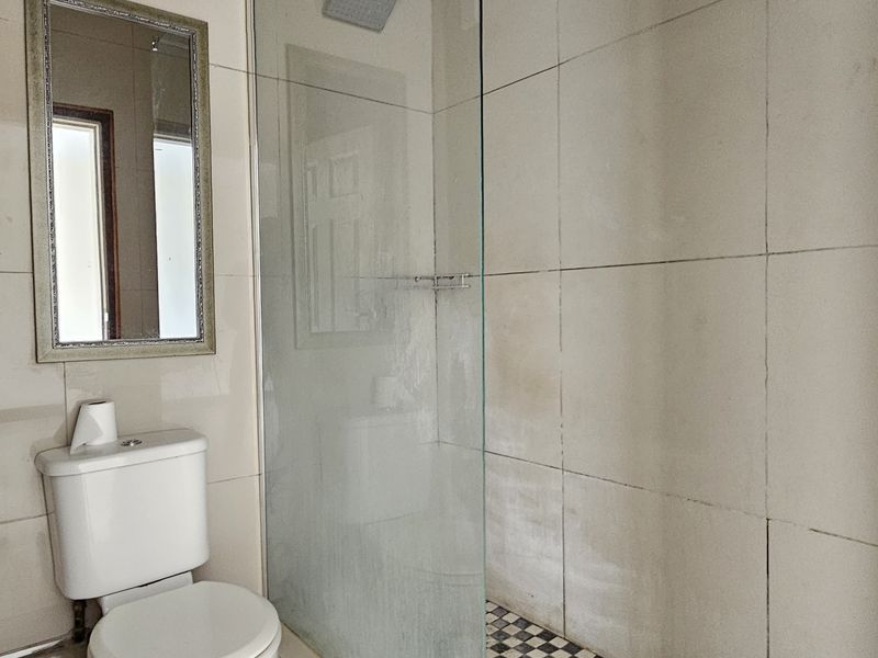 A functional bathroom featuring a glass-enclosed shower with a rainfall shower head, tiled walls, and a standard toilet.