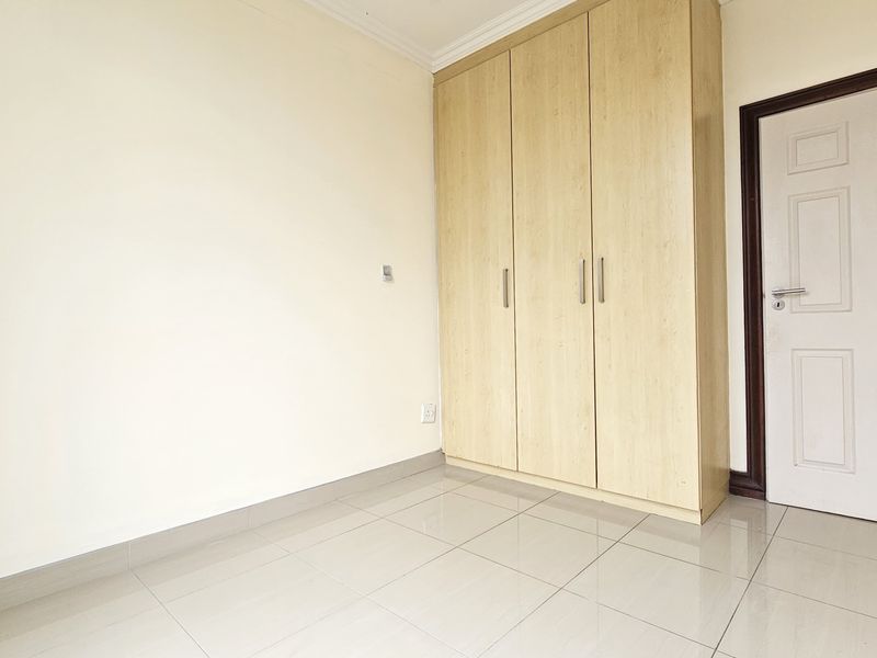 A clean, empty bedroom featuring light-toned tiled flooring and a modern built-in wardrobe with wood-grain finish.