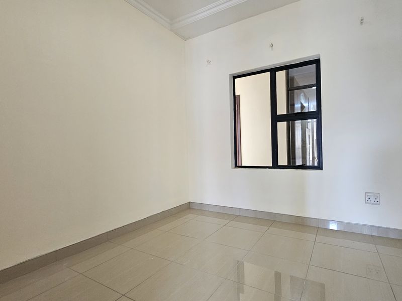 A clean, empty bedroom featuring neutral tiled flooring, white walls, and a modern black-framed window, providing a bright and versatile living space.