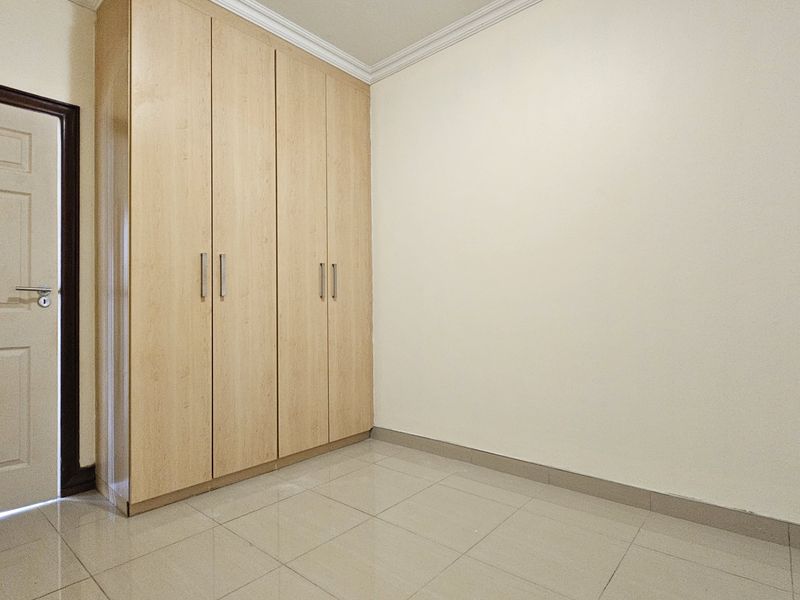A clean, empty bedroom featuring light wood-finish built-in wardrobes, neutral walls, and tiled flooring, providing a versatile space ready for personalization.