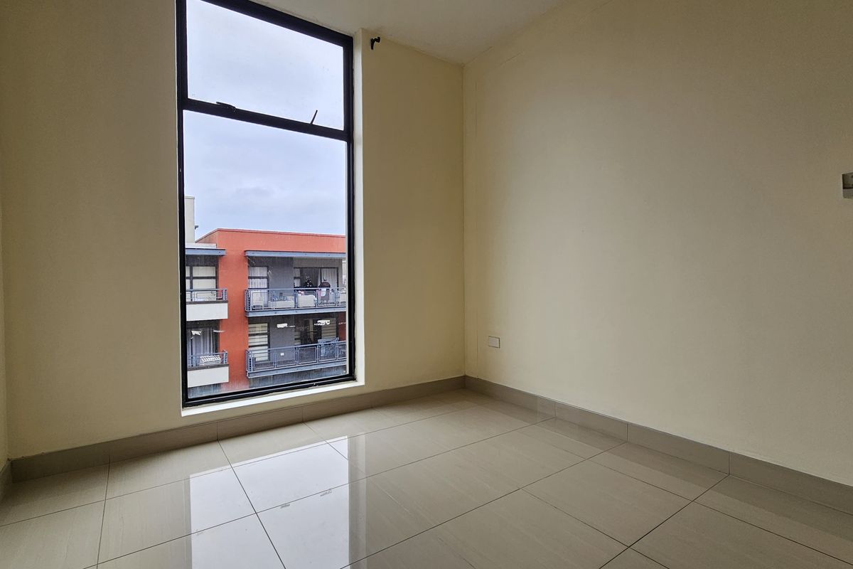 A bright, empty bedroom featuring large windows, neutral walls, and clean tiled flooring, offering a blank canvas for personalization.