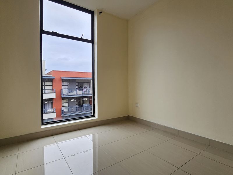 A bright, empty bedroom featuring large windows, neutral walls, and clean tiled flooring, offering a blank canvas for personalization.