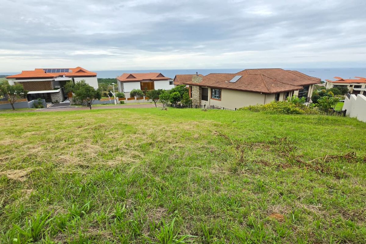 A view of a sloped residential vacant land plot overlooking neighboring properties and the distant ocean horizon.
