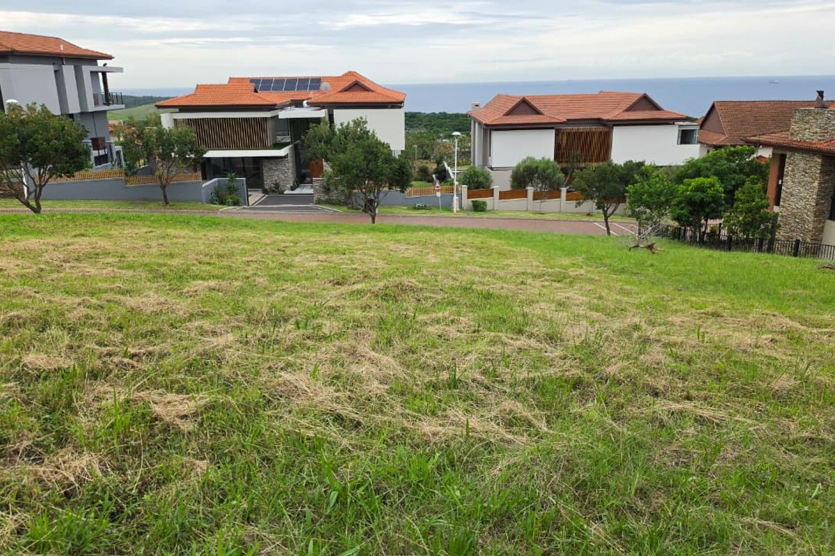 A vacant residential plot featuring a gentle slope, situated in a developed estate with established neighboring homes and street access.