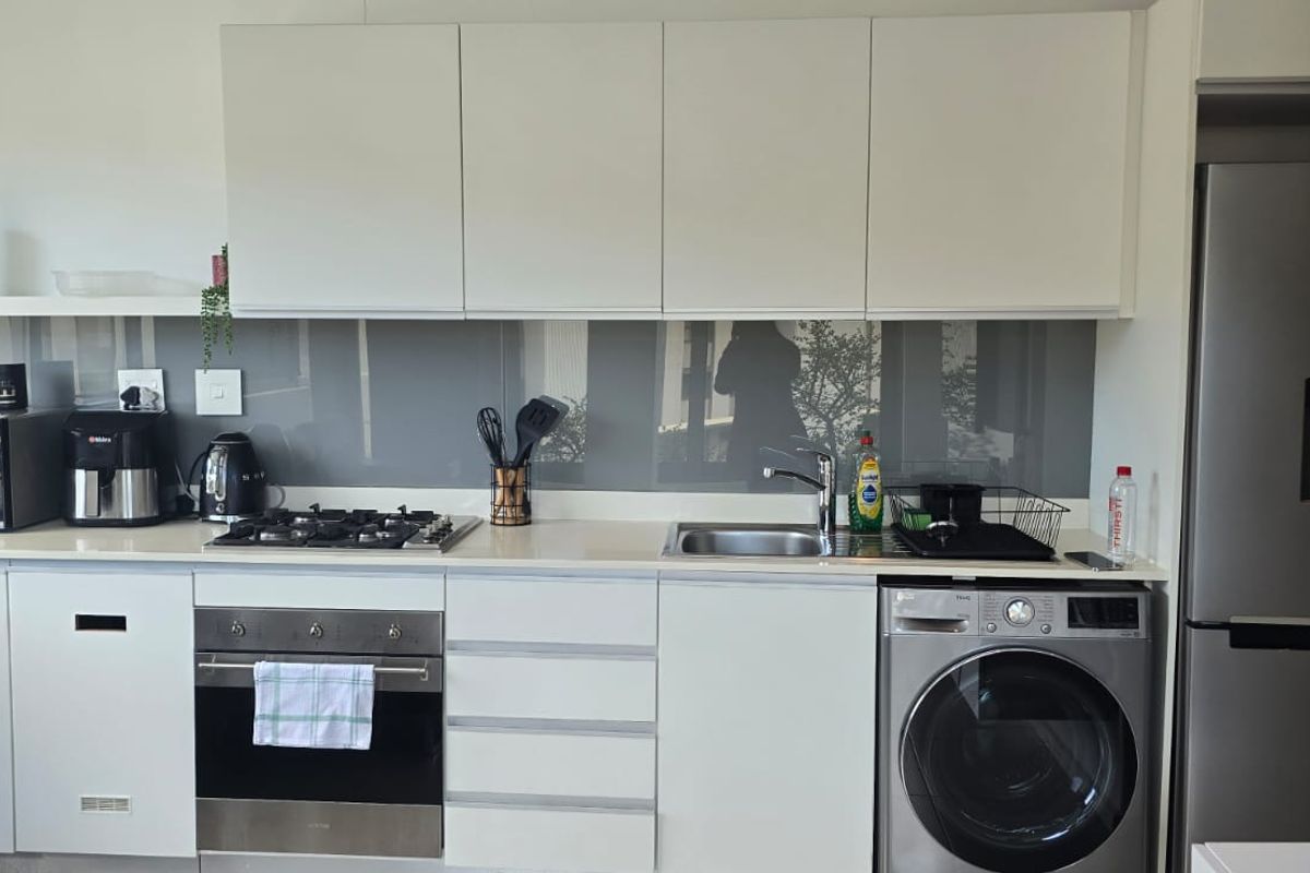 Modern kitchen featuring white cabinetry, stone countertops, a gas hob, built-in oven, integrated washing machine, and a sleek glass splashback.