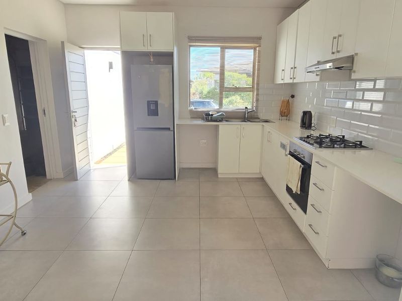 Modern kitchen featuring white cabinetry, subway tile backsplash, gas hob, built-in oven, and tiled flooring with direct access to the exterior.