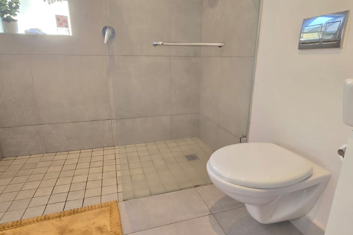 Modern bathroom featuring a walk-in shower with glass screen, wall-mounted toilet with concealed cistern, and contemporary grey tiling throughout.