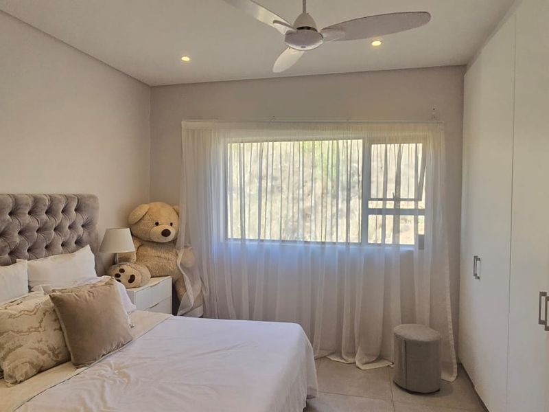 A well-maintained bedroom featuring neutral tiled flooring, recessed ceiling lighting, a modern ceiling fan, and ample built-in cupboard storage.