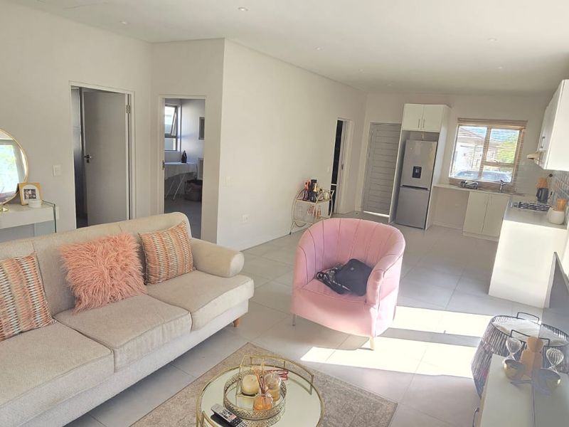 An open-plan living and kitchen area featuring neutral tiled flooring, modern cabinetry, and a functional layout with direct access to adjacent rooms.