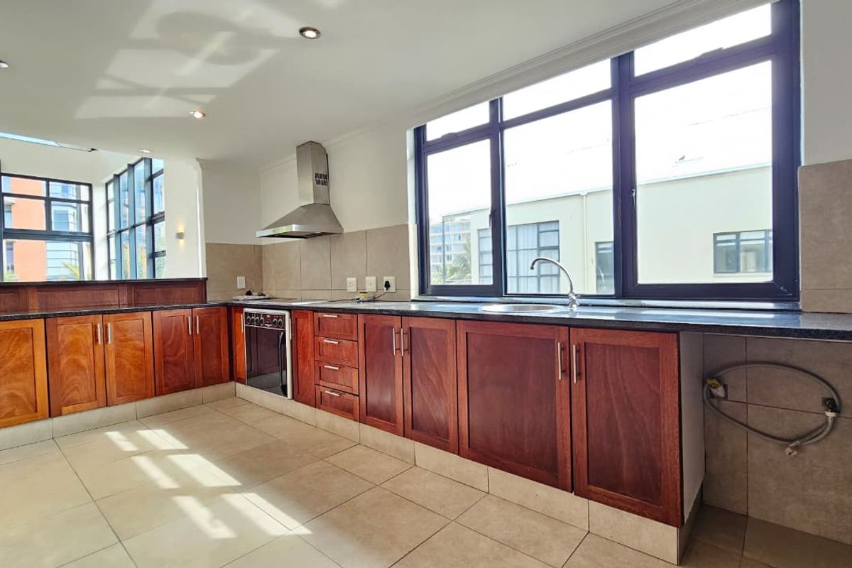 Spacious kitchen featuring warm-toned wooden cabinetry, granite countertops, built-in oven, stainless steel extractor fan, and large windows providing ample natural light.