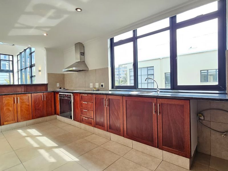 Spacious kitchen featuring warm-toned wooden cabinetry, granite countertops, built-in oven, stainless steel extractor fan, and large windows providing ample natural light.