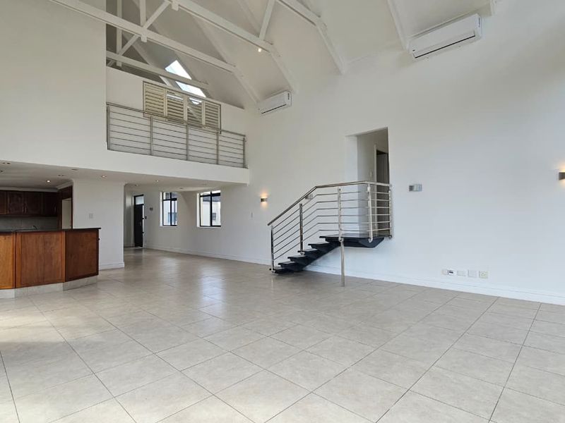 Spacious open-plan living area featuring a vaulted ceiling, mezzanine level, tiled flooring, and a built-in kitchen, offering a bright and airy penthouse atmosphere.