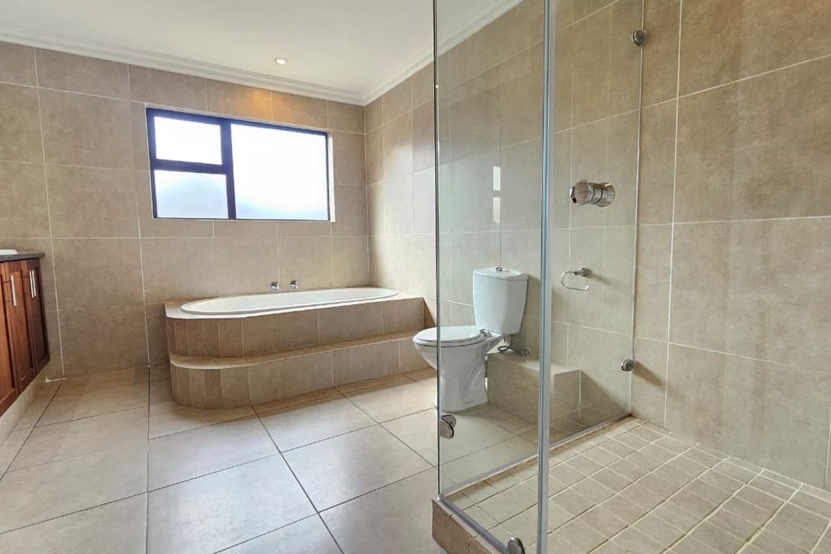 Spacious bathroom featuring a built-in bathtub, glass-enclosed shower, toilet, and vanity cabinet with neutral floor-to-ceiling tiling.