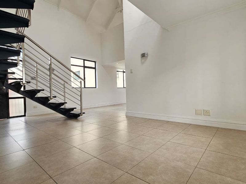 Spacious open-plan living area featuring high vaulted ceilings, a modern metal staircase with stainless steel balustrades, and neutral tiled flooring throughout.