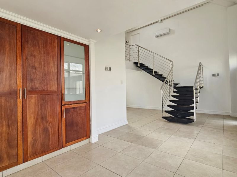 Spacious living area featuring tiled flooring, built-in wooden cabinetry, and a modern staircase with a metal balustrade.