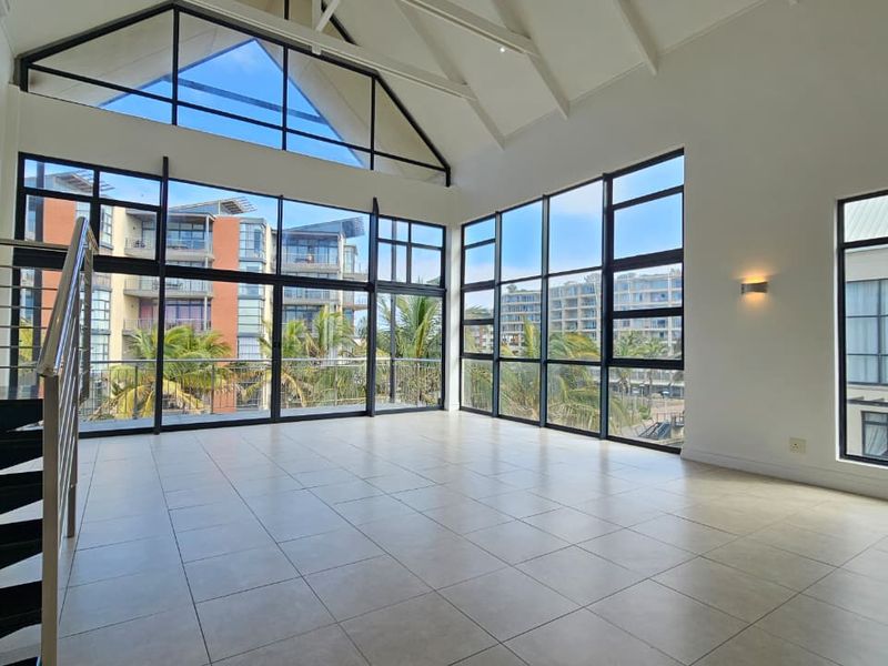 Spacious, light-filled living area featuring a vaulted ceiling, large windows with expansive views, and a modern staircase with metal balustrades.