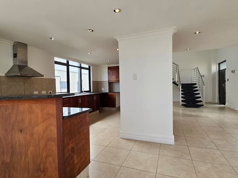 Spacious open-plan kitchen and living area featuring wooden cabinetry, granite countertops, tiled floors, and a modern staircase leading to the upper level.