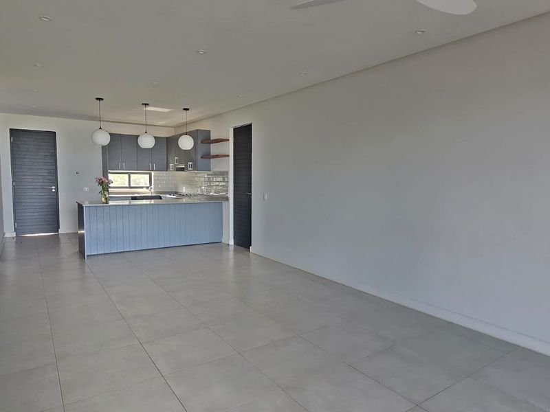 Spacious open-plan living area featuring a modern kitchen with a central island, sleek cabinetry, and neutral tiled flooring throughout.
