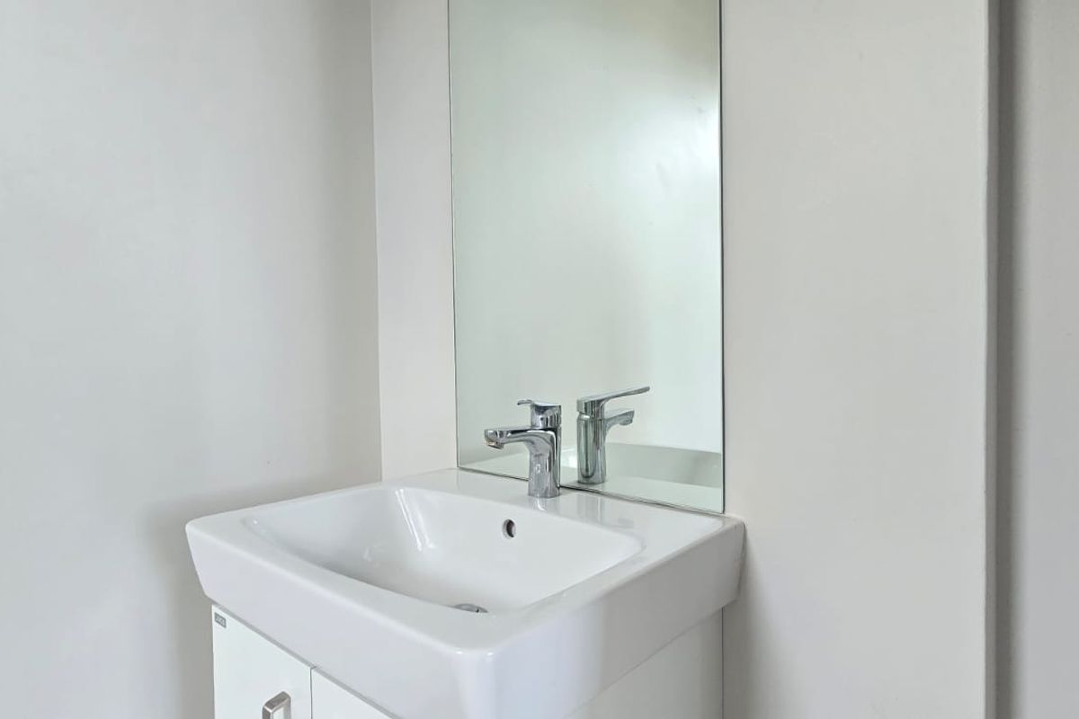 A clean and minimalist bathroom vanity featuring a white cabinet, ceramic basin, chrome mixer tap, and a wall-mounted mirror.