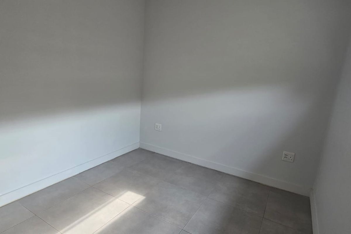 A clean, empty bedroom featuring neutral tiled flooring, white walls, and a window fitted with modern blinds.