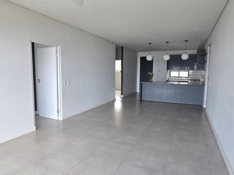 Spacious open-plan living and kitchen area featuring modern grey cabinetry, a central island, tiled flooring, and neutral finishes throughout.