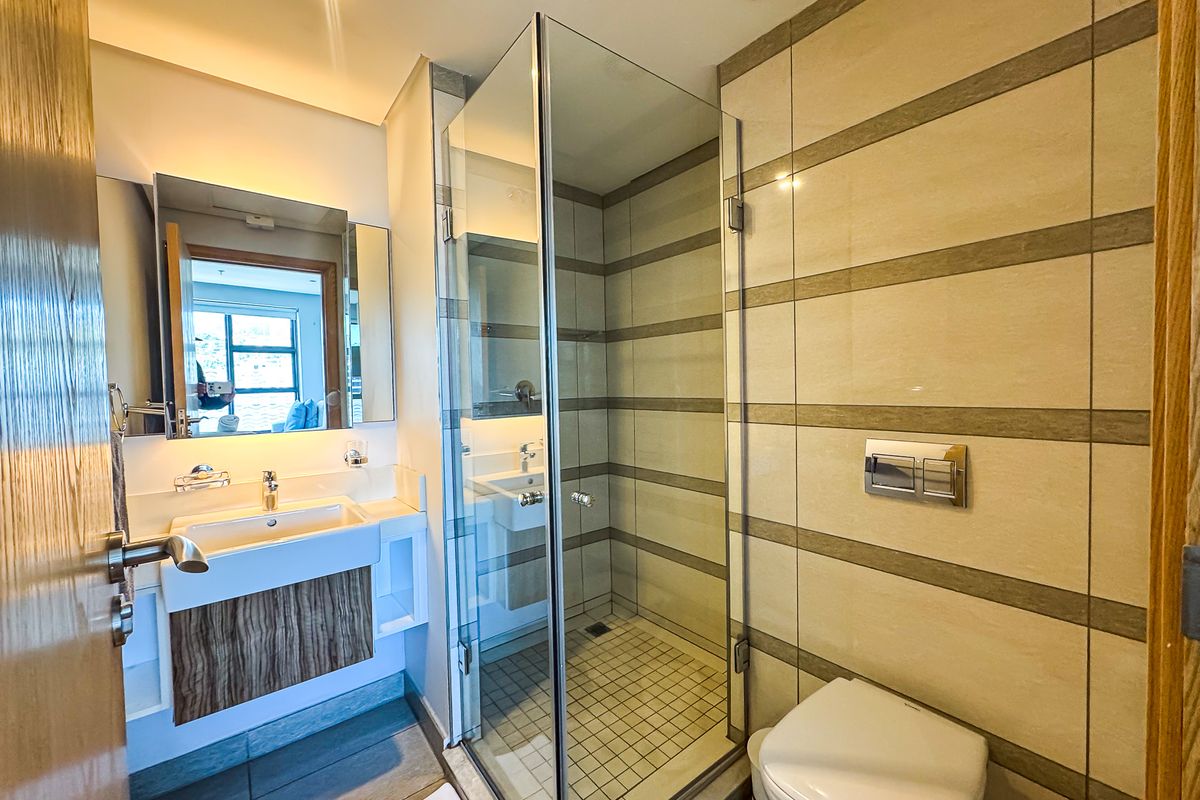 Modern bathroom featuring a wall-mounted vanity, glass-enclosed shower, and wall-hung toilet with neutral tiled finishes.