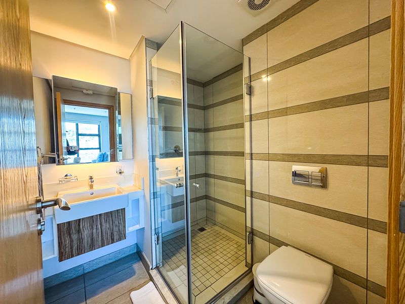Modern bathroom featuring a wall-mounted vanity, glass-enclosed shower, and wall-hung toilet with neutral tiled finishes.